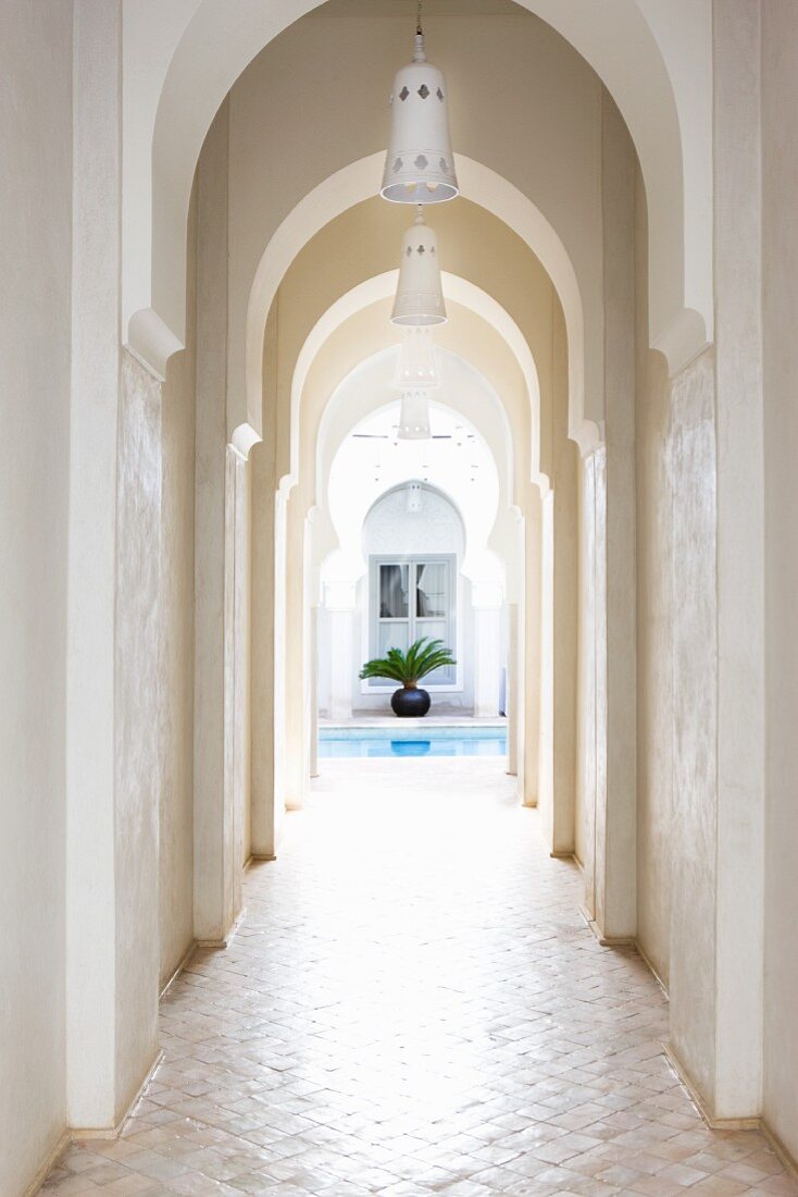 Schmaler Bogengang in Eingangsbereich eines marokkanischen Hauses mit Blick auf Wasserbecken und Palme im Innenhof