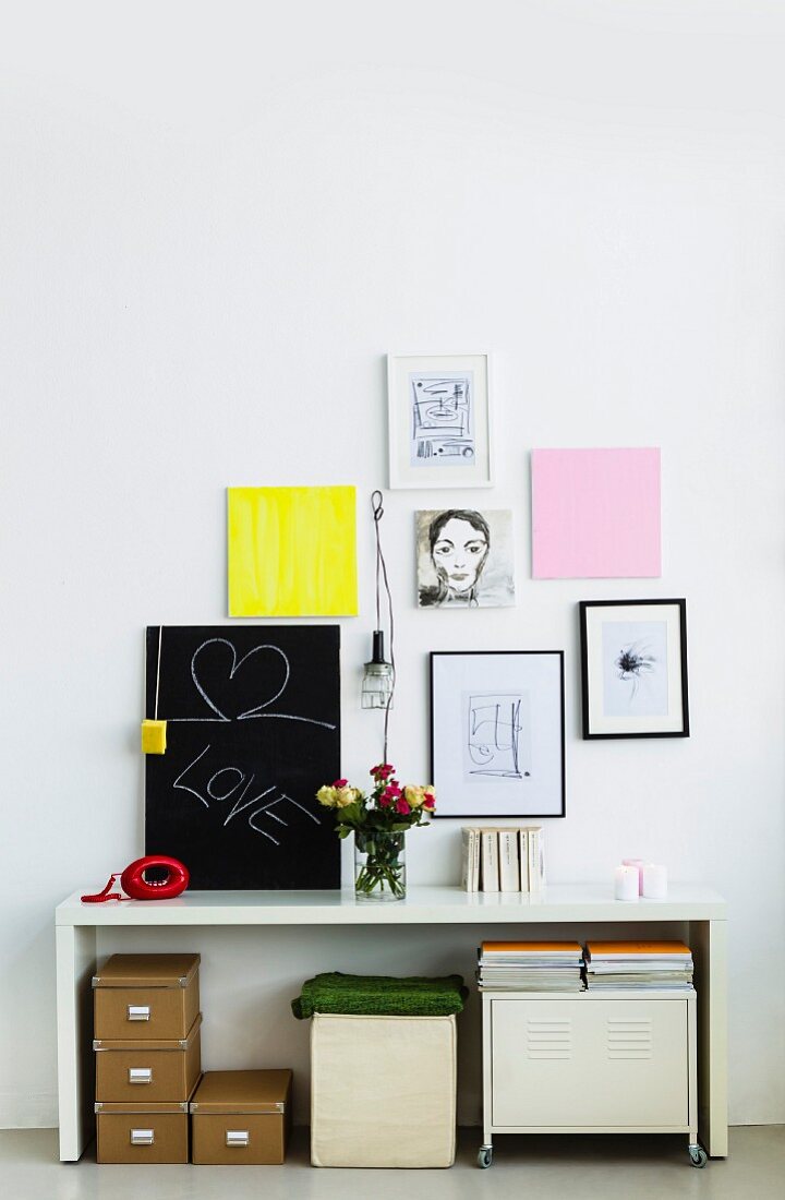 Archive boxes next to stool and cabinet under white desk below pictures hanging on wall