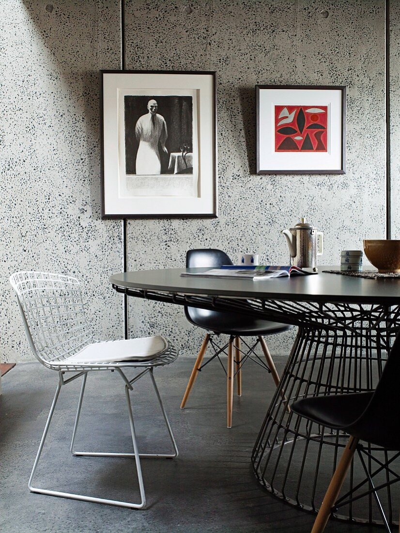 Verschiedene Bauhausstühle um runden Tisch vor grauen Wandpaneelen mit gerahmten Bildern