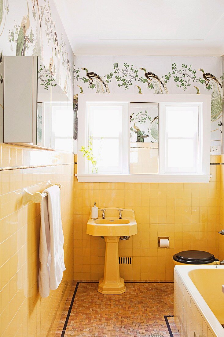 Vintage bathroom with pedestal sink against yellow wall tiles below stencilled frieze with bird motif
