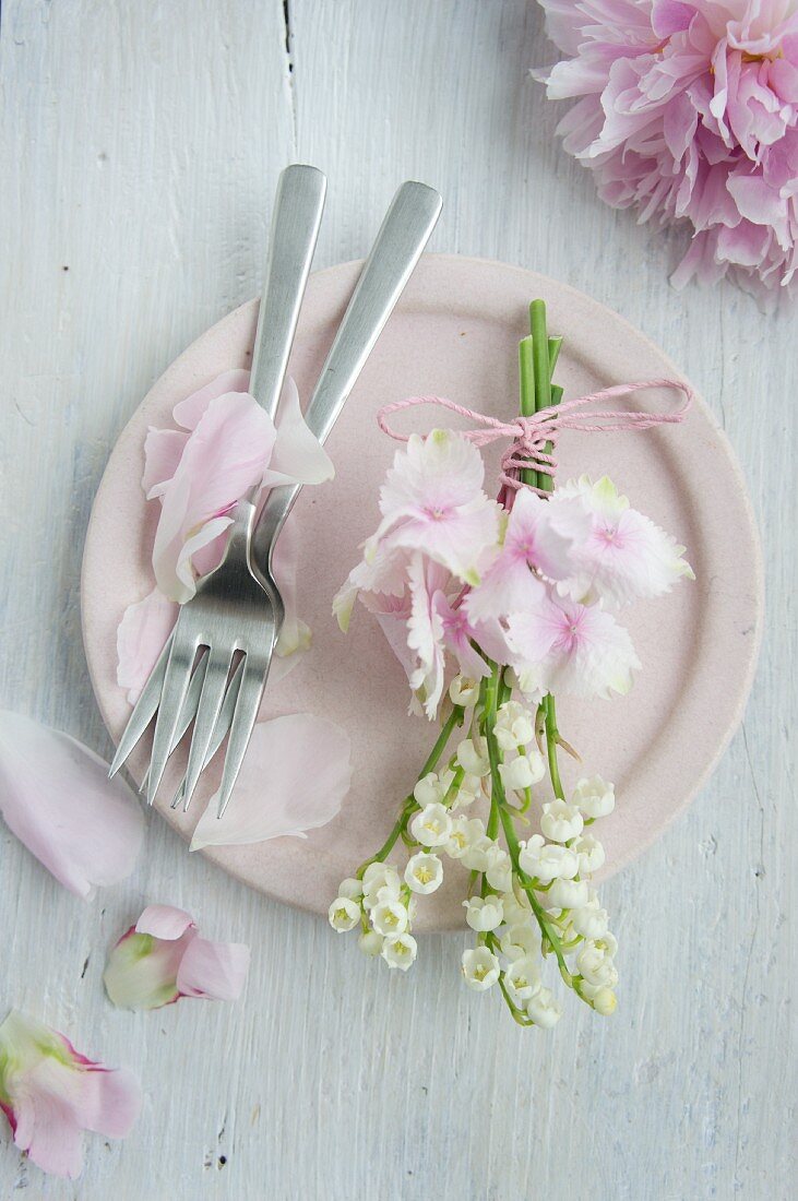 Posy of lily-of-the-valley and hydrangeas on pink plate scattered with peony petals