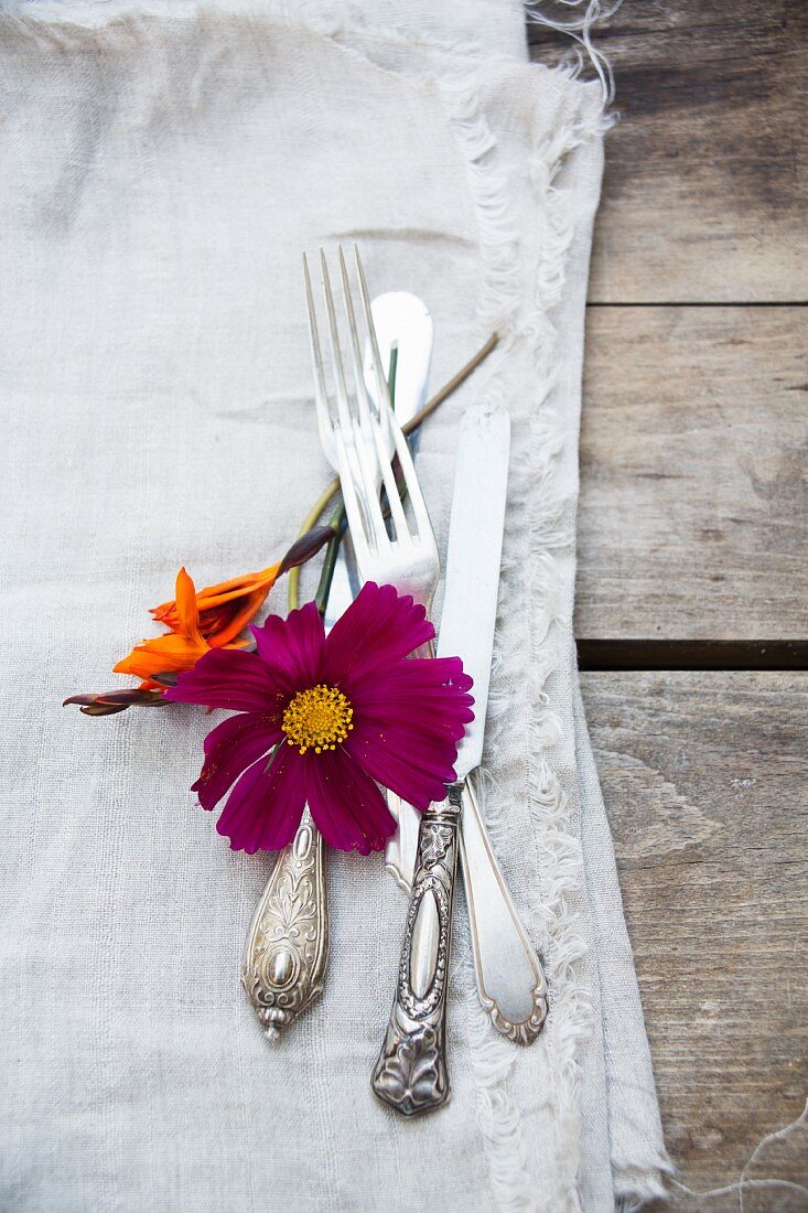 Silver cutlery, flowers and linen napkin on wooden table