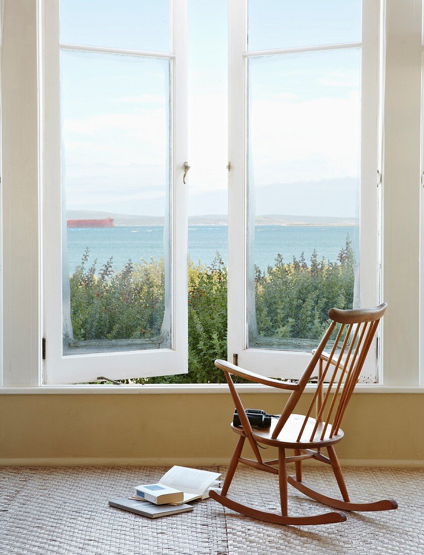 Schlichter Schaukelstuhl aus Holz vor Fenster mit Meerblick