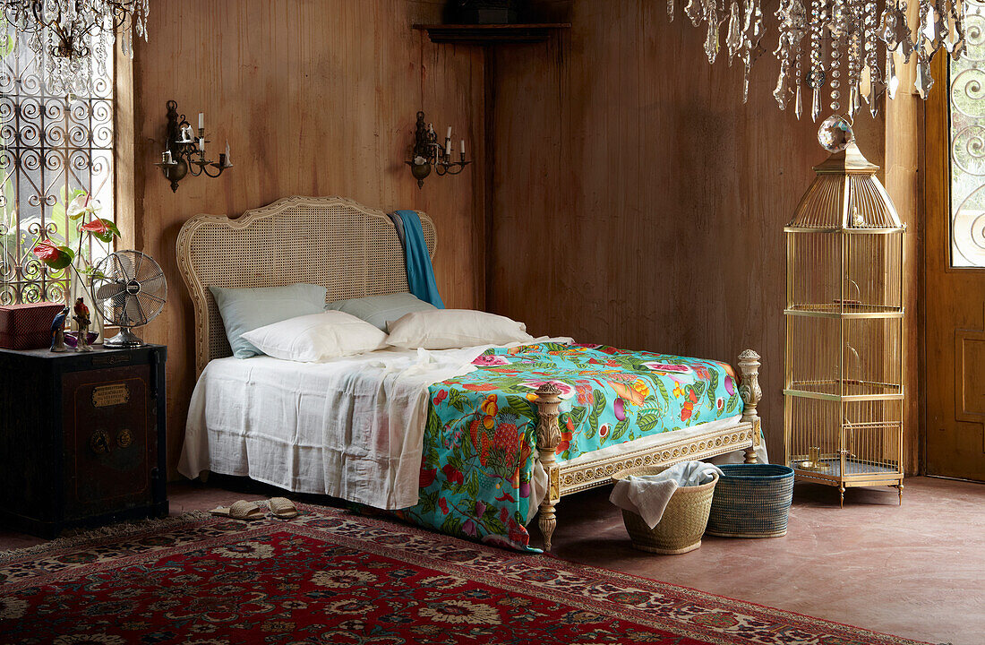 Rattanbett mit bunter Tagesdecke und Vogelkäfig im Schlafzimmer mit Holzverkleidung