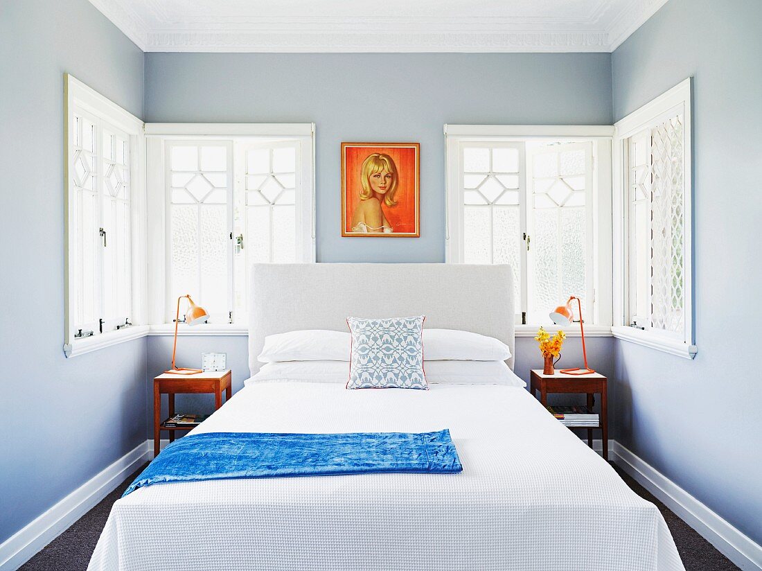 Schlichtes Doppelbett vor Fenster mit Ornamenten in schmalem Schlafzimmer, hellgraue Wände und gemaltes Frauenportrait im Retrostil
