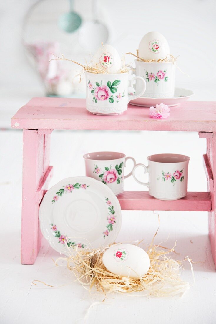 Floral-patterned cups and Easter decorations on pink footstool