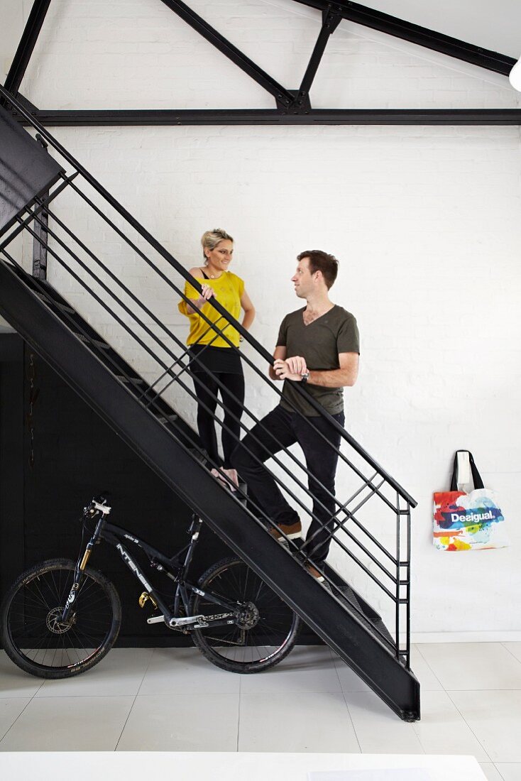 Frau und Mann auf schwarzer Metalltreppe, darunter Fahrrad, in einer Loft-Wohnung