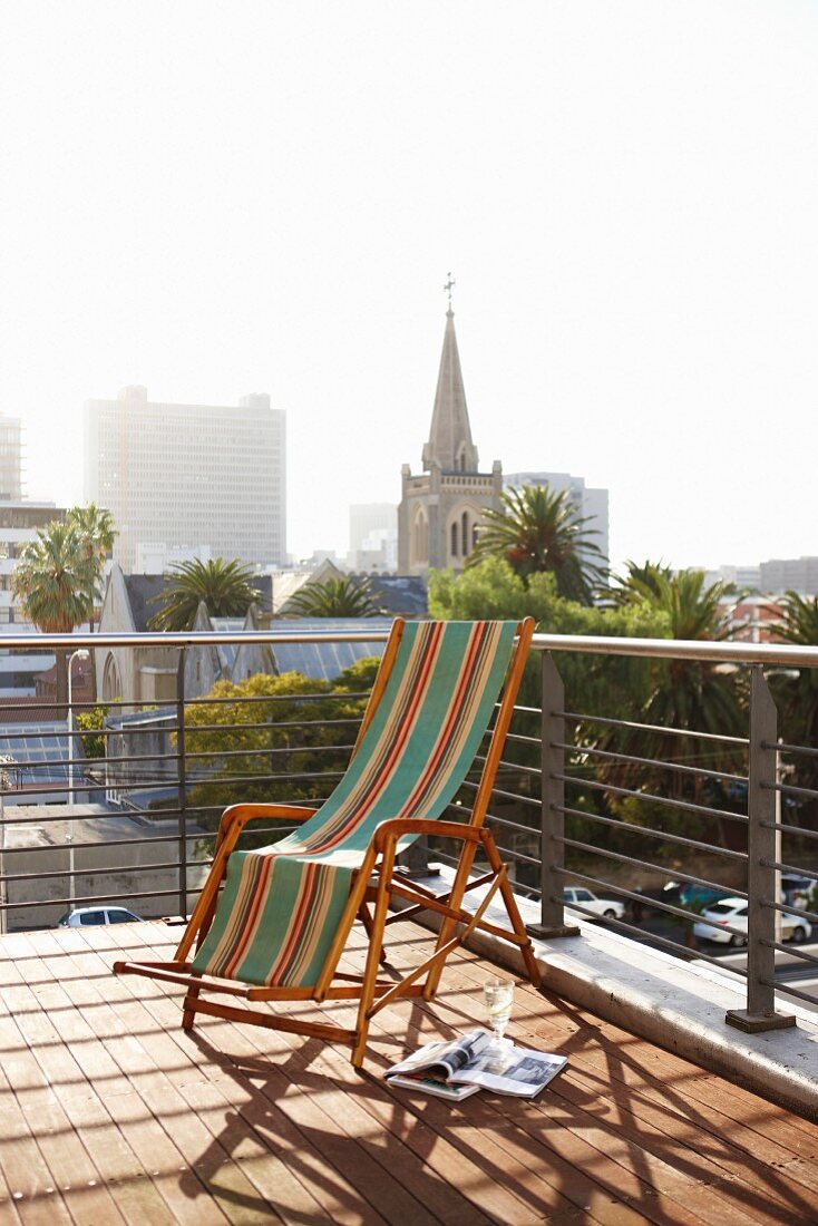 Striped, vintage deckchair on wooden deck with modern balustrade and view of Cape Town cityscape