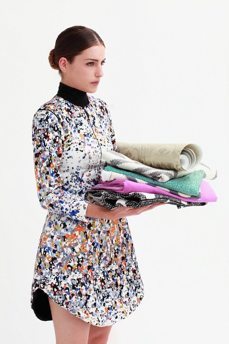 Woman wearing colourful pixelated dress holding stack of patterned fabrics