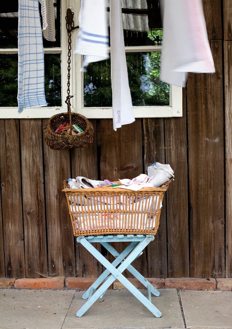 Wäschekorb auf Klapphocker vor rustikalem Holzhaus