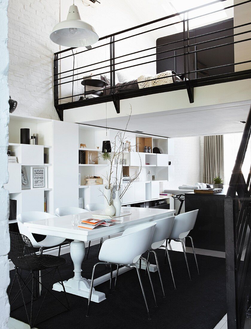 Wohnen auf kleinem Raum - weisser Holztisch und moderne Schalenstühle auf schwarzem Teppich in offenem Wohnraum mit Galerie