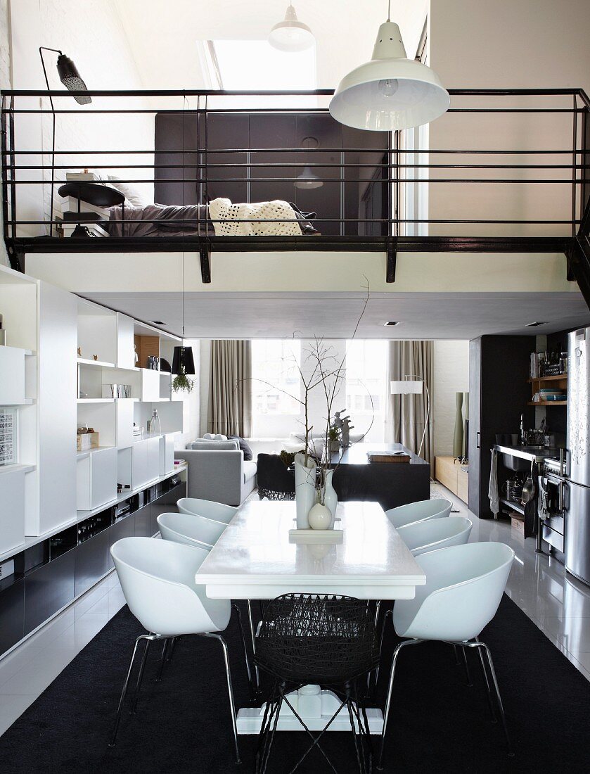 White dining set with modern shell chairs on black rug in narrow apartment with bedroom in mezzanine