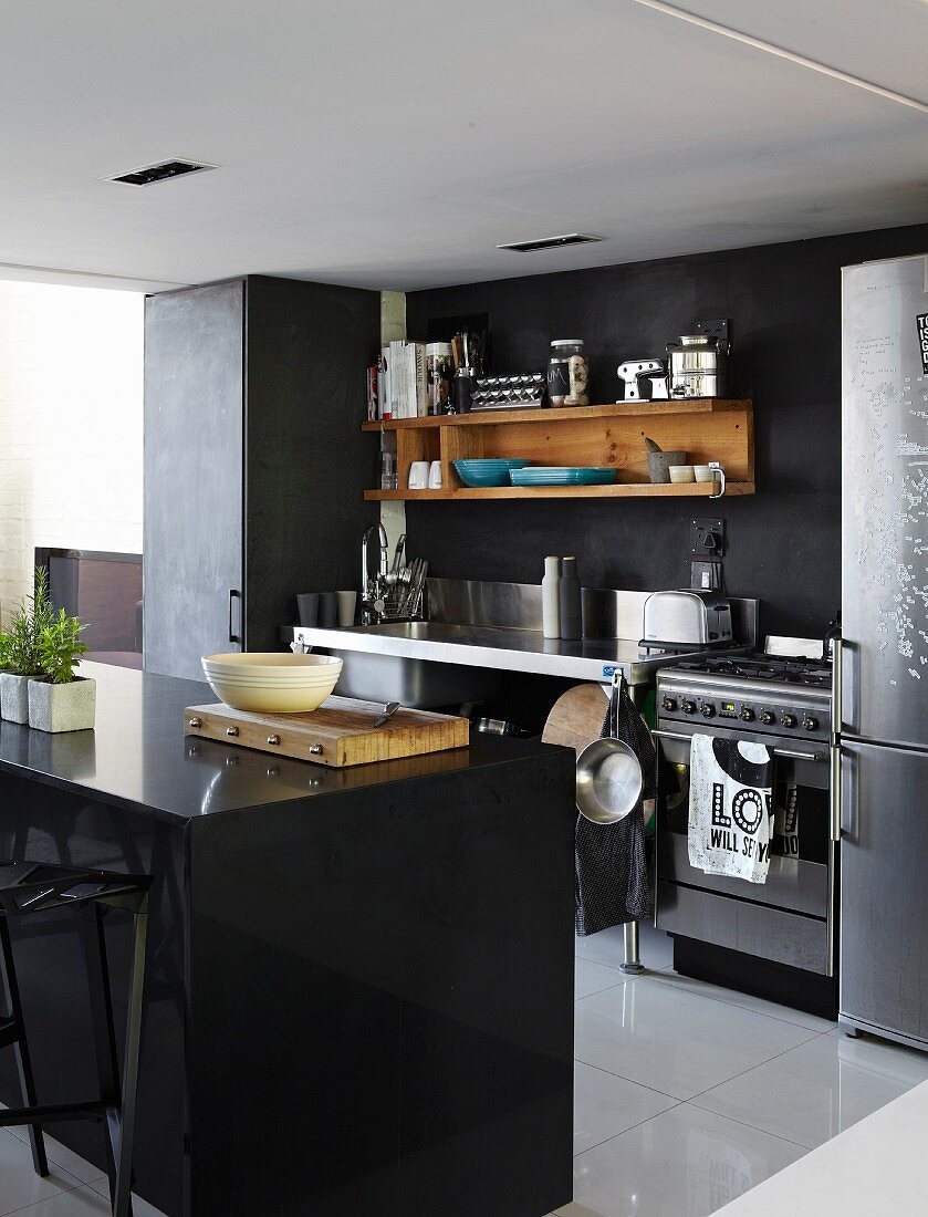 Schwarze Theke gegenüber werkbankartiger Küchenzeile und Holzboard an dunkler Wand