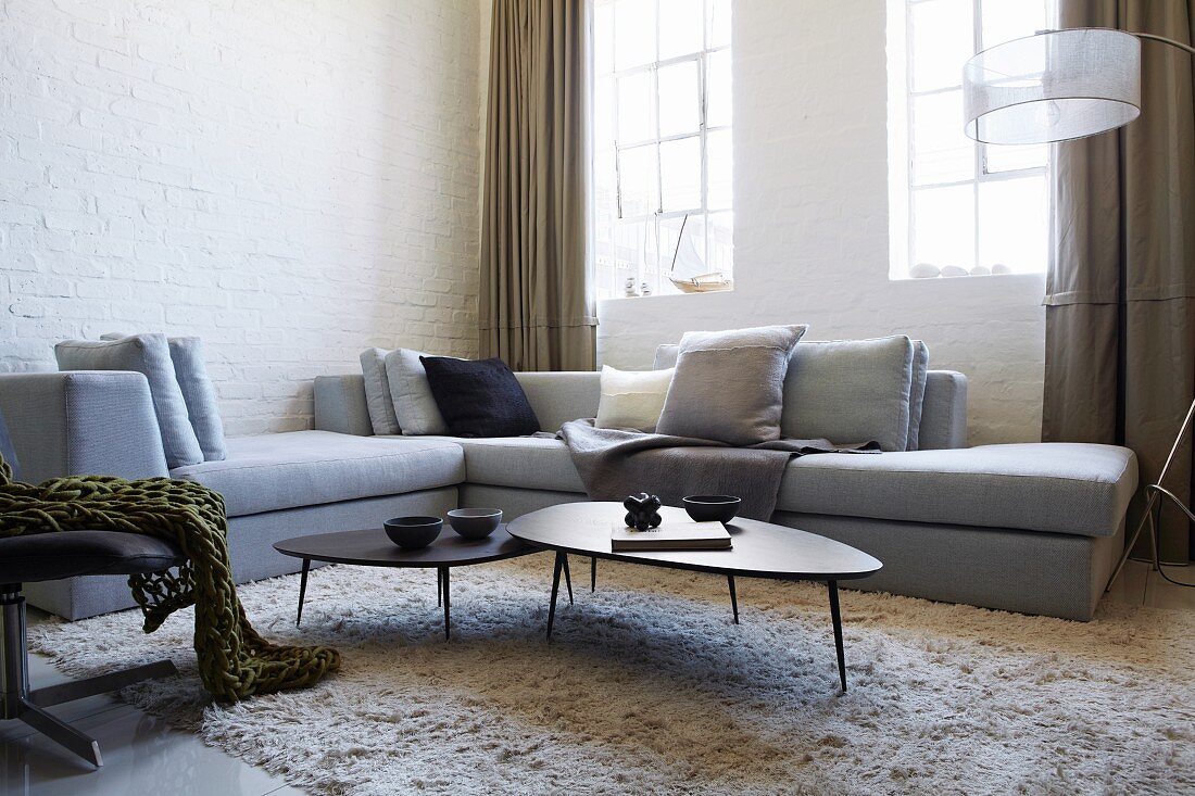 Pale grey corner sofa and fifties-style coffee table set on flokati-style rug in corner in front of lattice windows