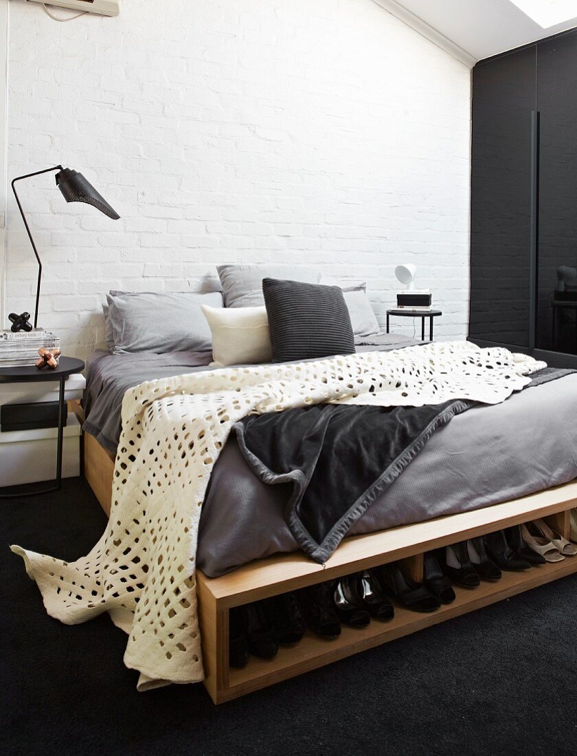 Weisses Plaid mit Lochmuster auf selbstgebautem Bett mit integriertem Schuhfach, rustikales Ambiente mit geweisselter Ziegelwand