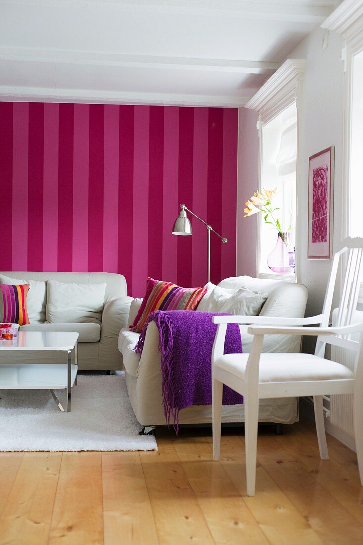 Sitzecke in skandinavischem Wohnzimmer mit weissen Möbeln vor rot-pink gestreifter Tapete