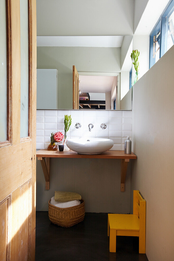 Guest bathroom with sink on wooden shelf, yellow children's chair in the foreground