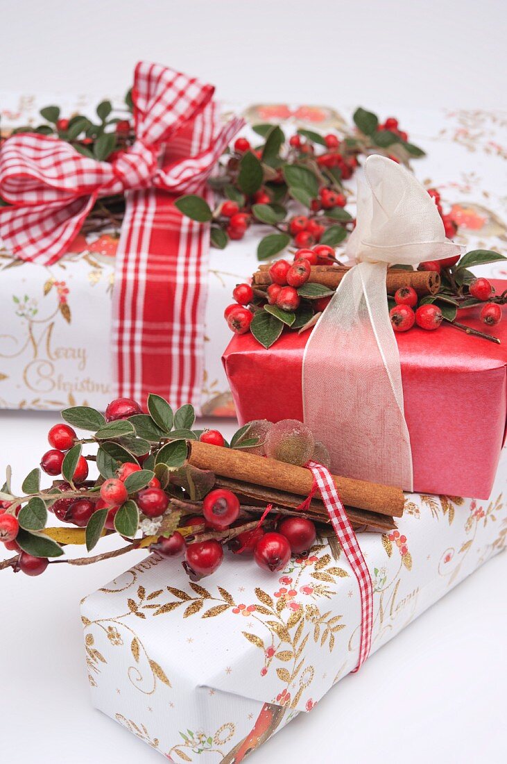 Weihnachtspäckchen, dekoriert mit Geschenkband, Hagebutten und Zimtstangen