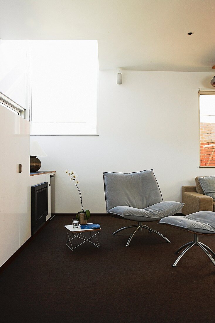 Sessel mit passendem Schemel auf dunklem Teppichboden in minimalistischem Zimmer