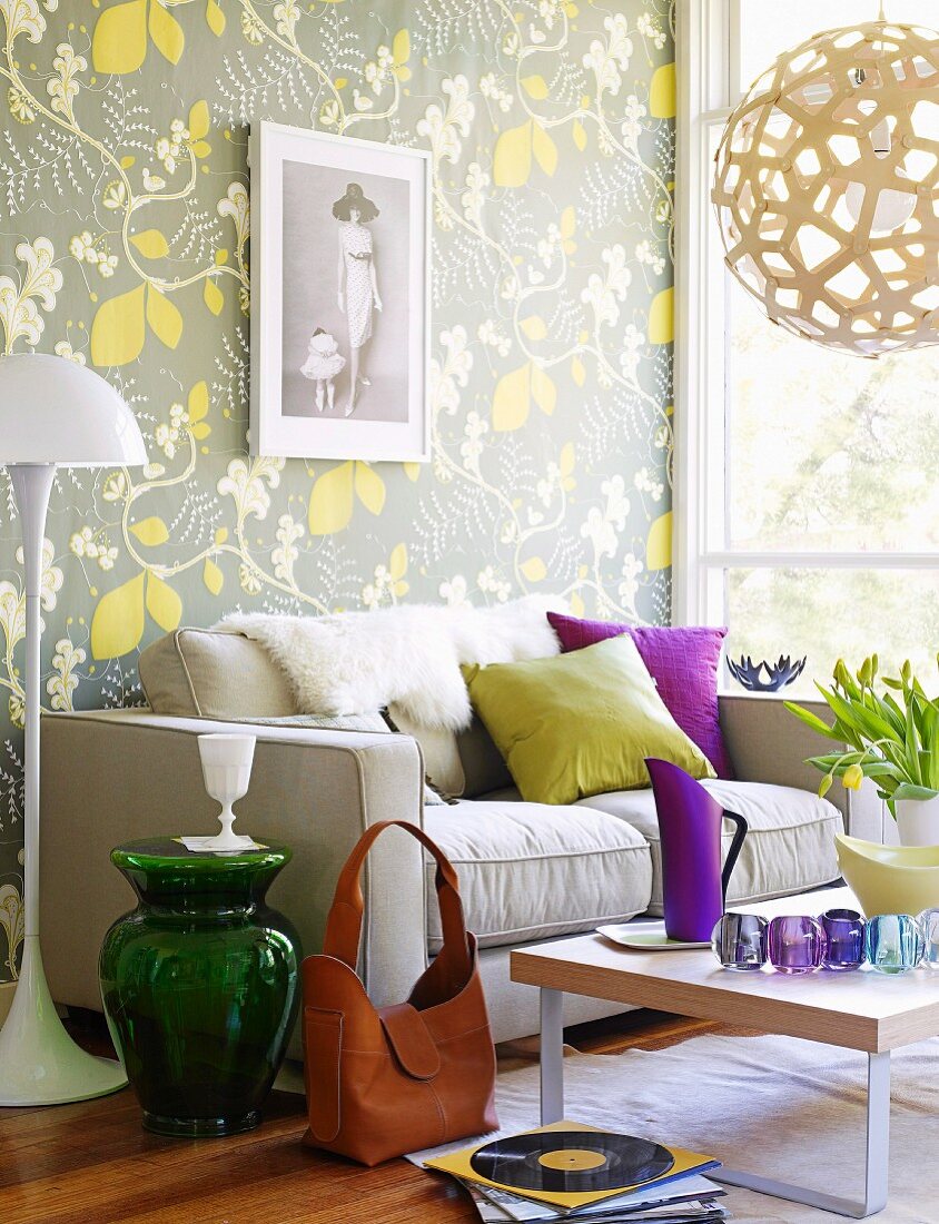 Sofa and standard lamp against wall with floral wallpaper