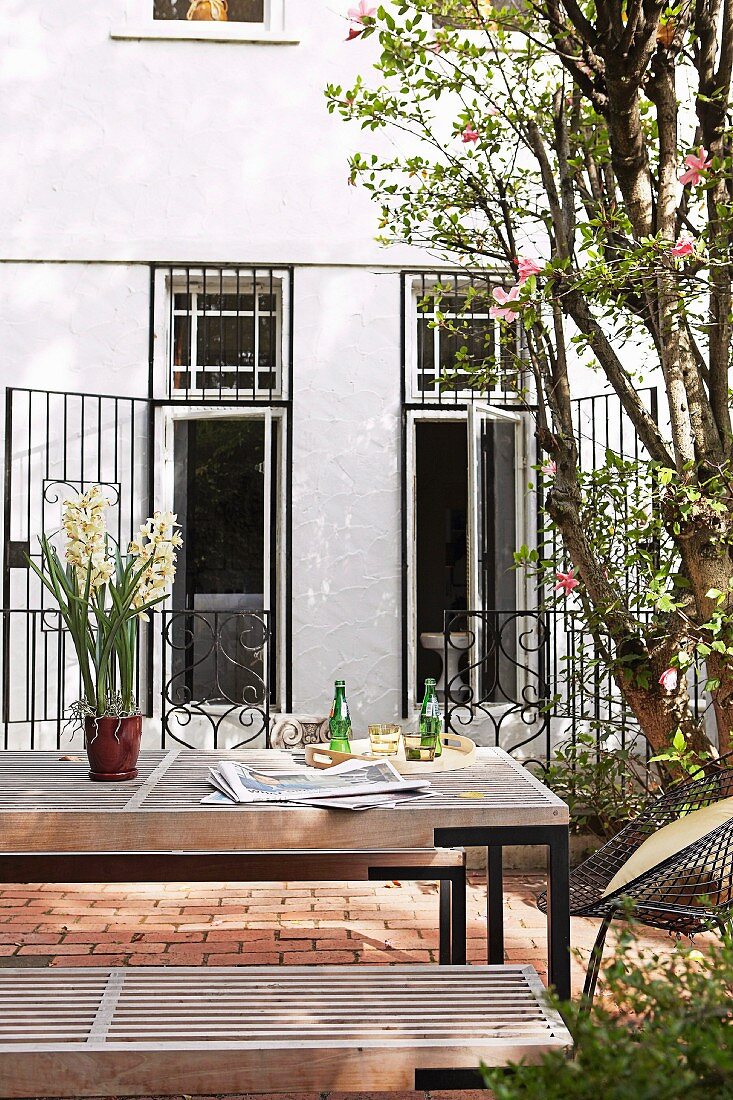 Moderne Outdoor-Tischgarnitur im Innenhof vor Wohnhaus mit offenem Gitter vor Terrassentüren