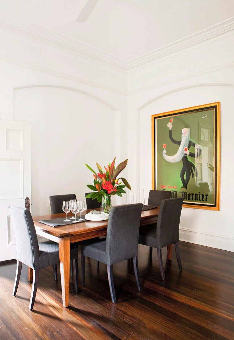 Graue Polsterstühle an elegantem Esstisch mit Blumenschmuck; grosses, gerahmtes Retro Plakat an der Wand in einer Stucknische