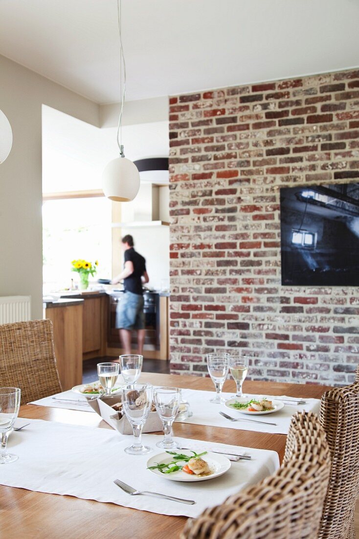 Set dining table in front of TV on old brick wall with view of open-plan kitchen in background