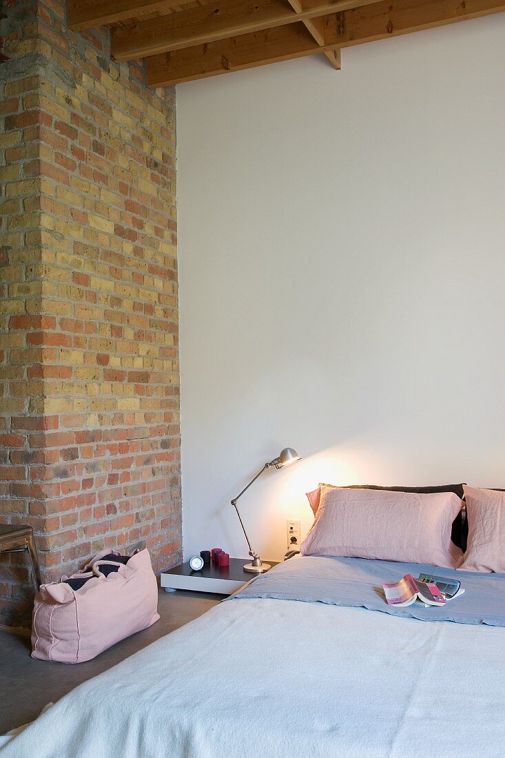 Bedside lamp next to simple bed in minimalist bedroom with brick wall