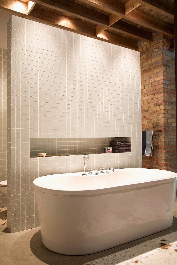 Free-standing bathtub against tiled partition with narrow niche in rustic interior