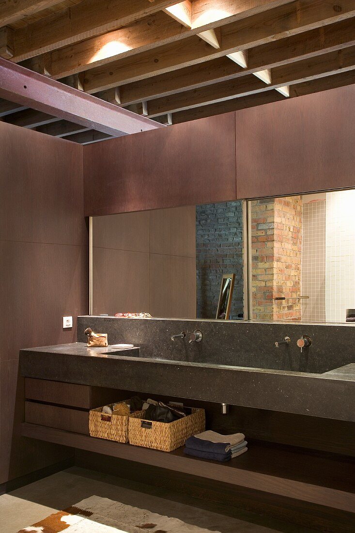 Trogartiger Waschtisch aus grauem Stein vor Spiegel im Badbereich, darüber sichtbare, durchgehende Tragkonstruktion