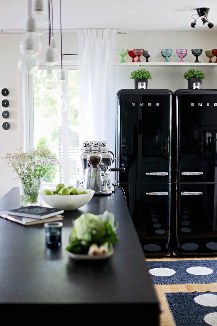 Dishes on counter with black worksurface and glossy, black, fifties-style fridges in background