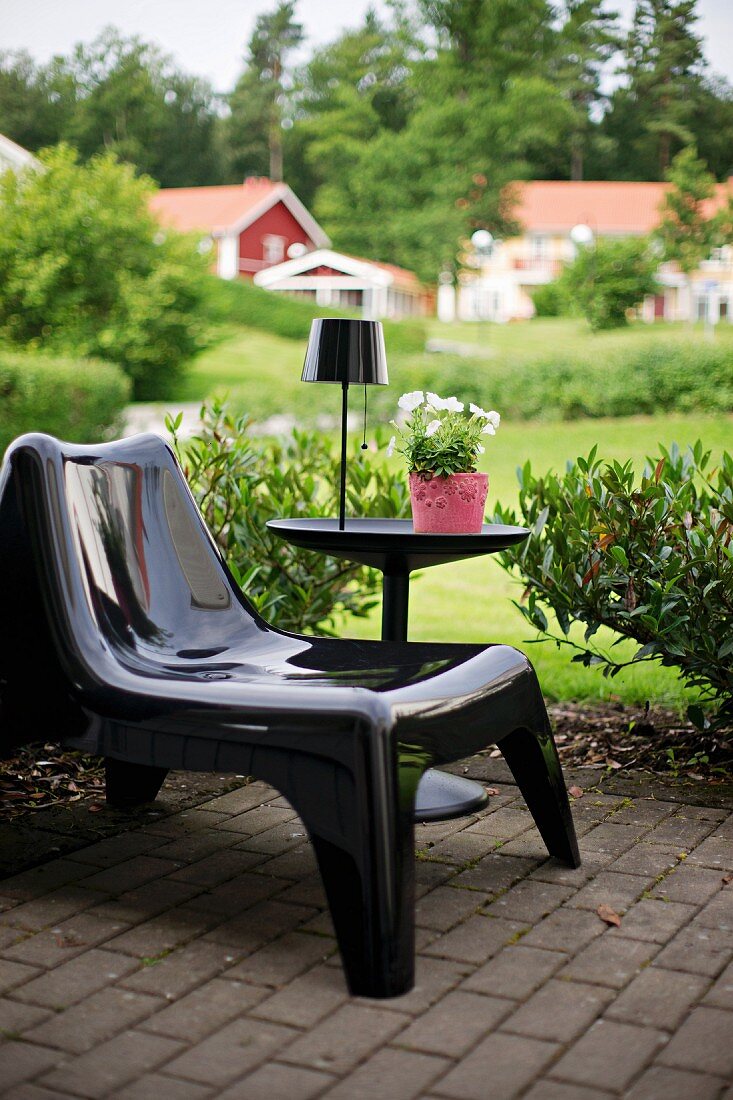 Schwarzer Kunststoff Sessel neben Beistelltisch mit schwarzer Tischleuchte auf Terrasse