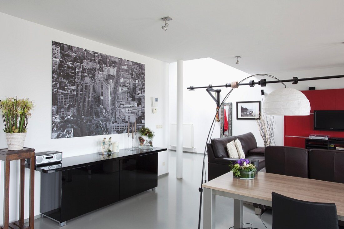 Moderne Loftwohnung, Bogenlampe mit weißem Papierschirm über Esstisch, gegenüber schwarzes Sideboard mit großformatigem Foto an Wand