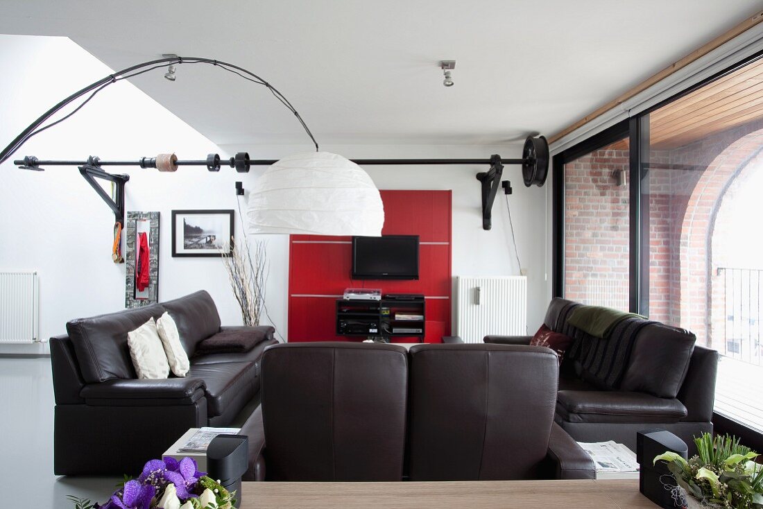 Schwarze Ledersofagarnitur in Loungebereich, davor Bogenlampe mit weißem Papierschirm in Loftwohnung