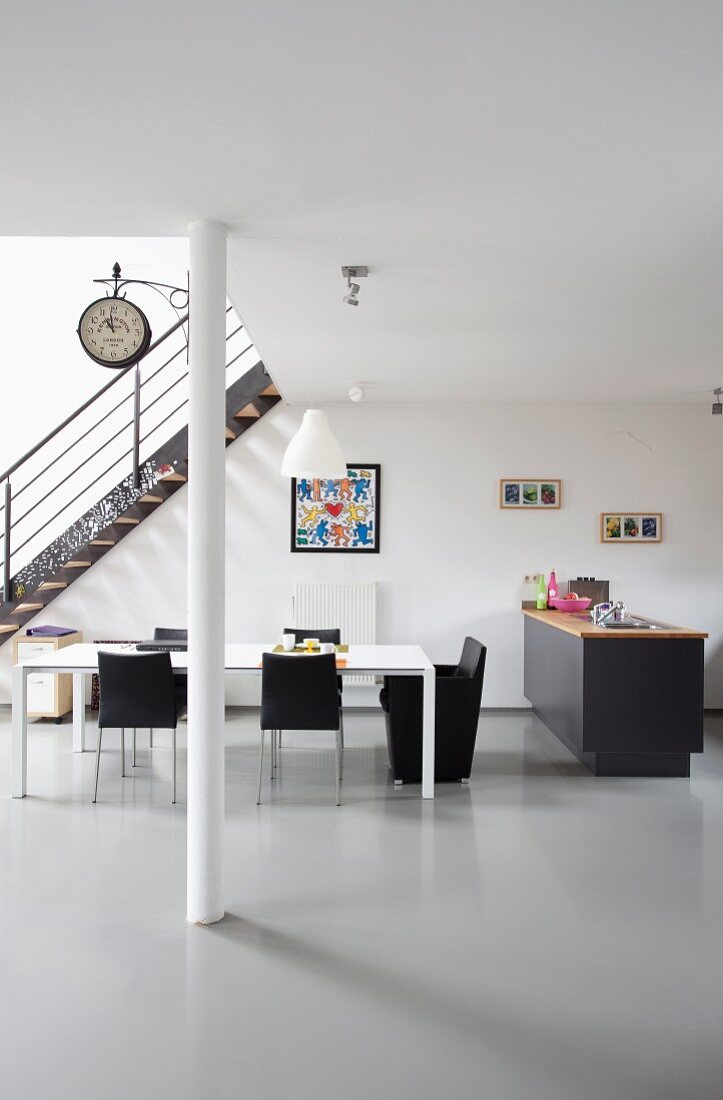 Minimalistische Loftwohnung mit Retro Charme, schwarze Stühle um weißem Esstisch neben Küchentheke mit dunkelgrauem Unterschrank