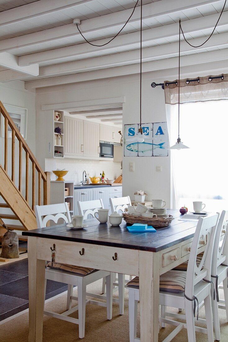 Rustikaler Esstisch und weiße Holzstühle in offenem Wohnraum mit maritimen Flair