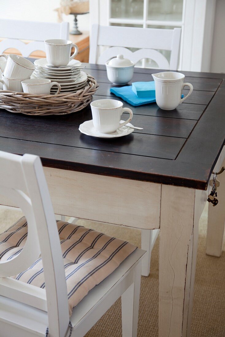 Kaffeegeschirr auf rustikalem Esstisch mit dunkler Holzplatte und weisser Holzstuhl mit Sitzkissen