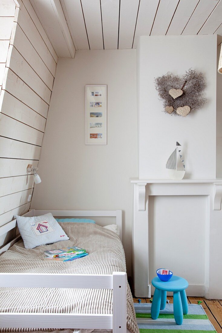 Kinderzimmer unter dem Dach mit weisser Holzverkleidung, blauer Schemel neben Bett