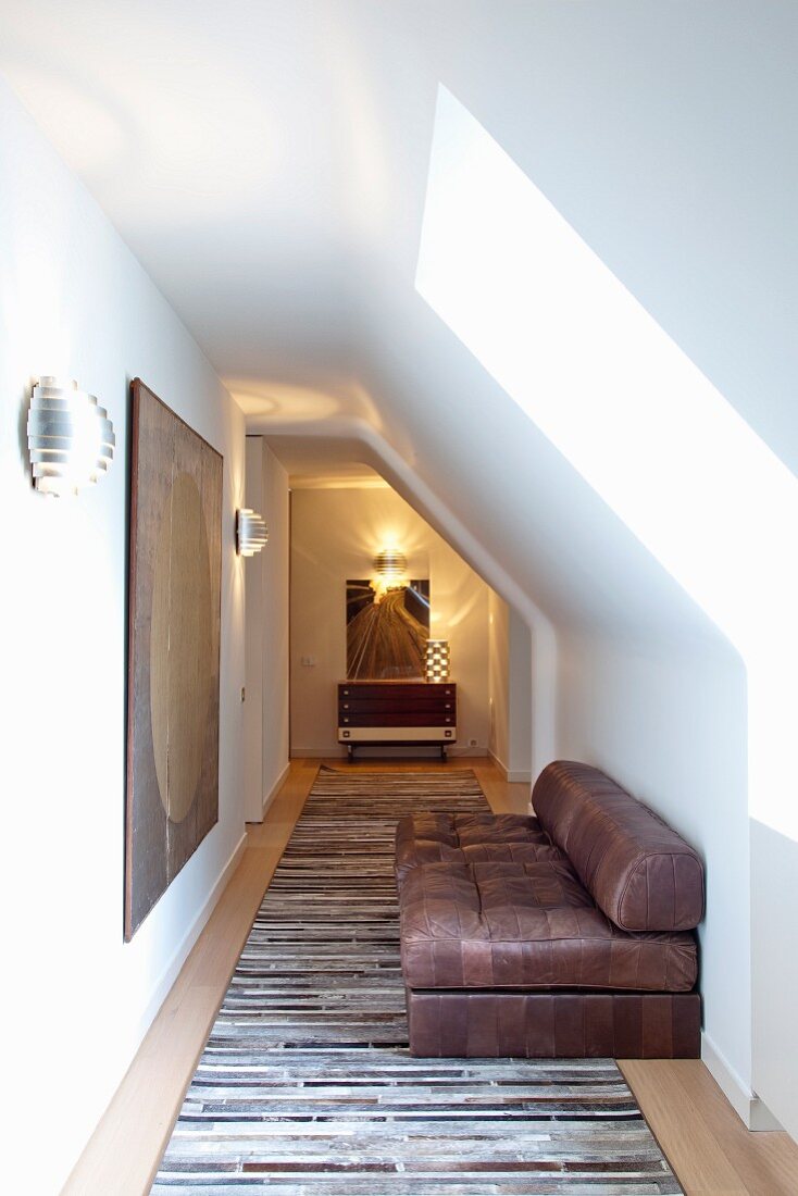 Brown leather sofa on rug in narrow hallway under sloping attic ceiling