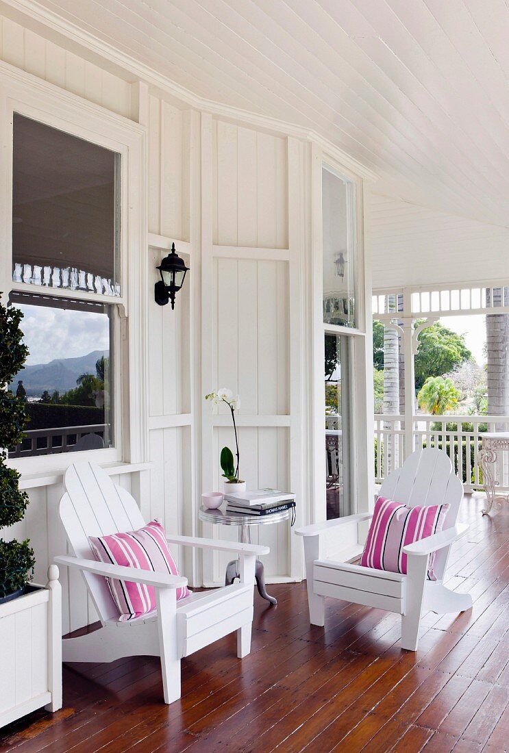 weiße Holzstühle mit Streifenkissen auf Veranda eines Landhauses im Kolonialstil