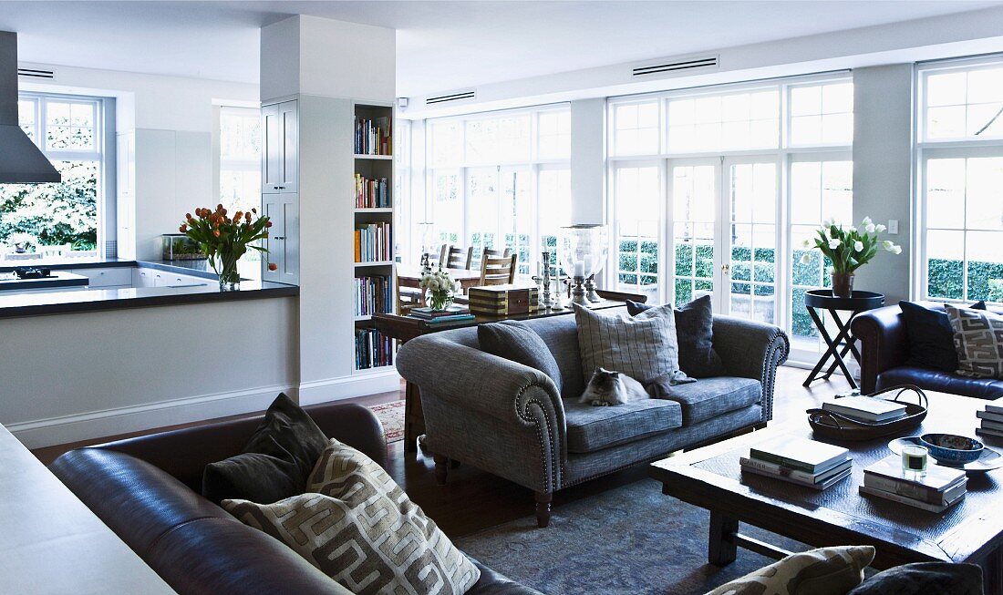 Traditional grey sofa and two leather sofas around coffee table in spacious, open-plan interior