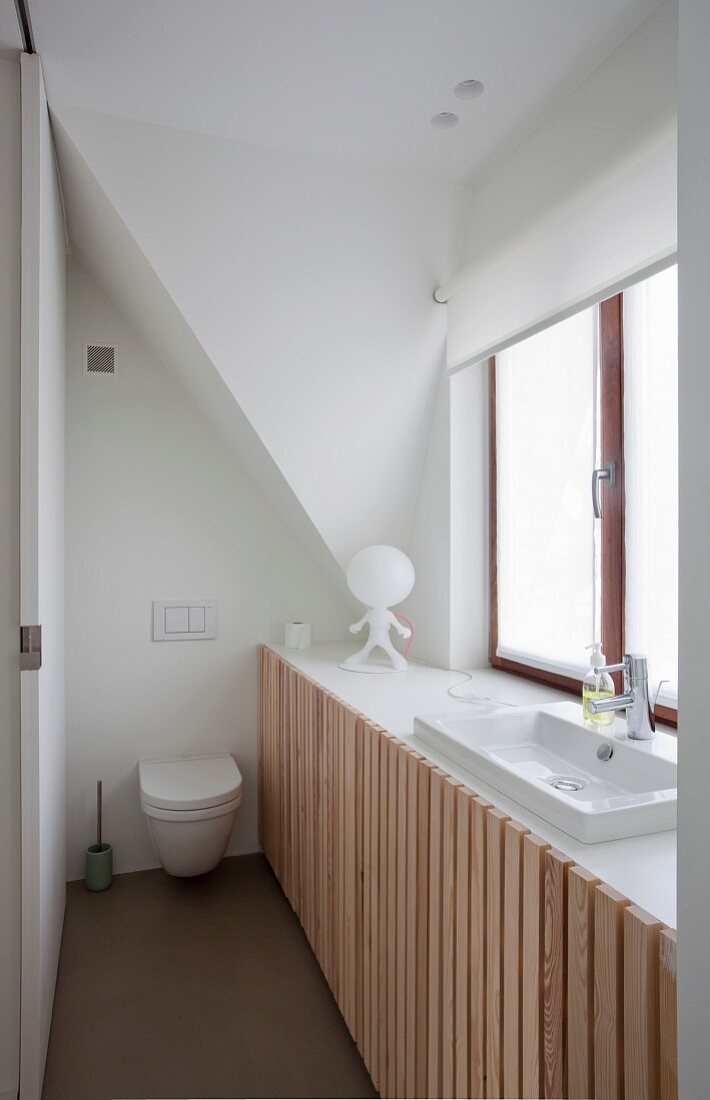 Space-saving bathroom; fitted cupboards with vertical slatted doors and integrated sink below window and toilet in background