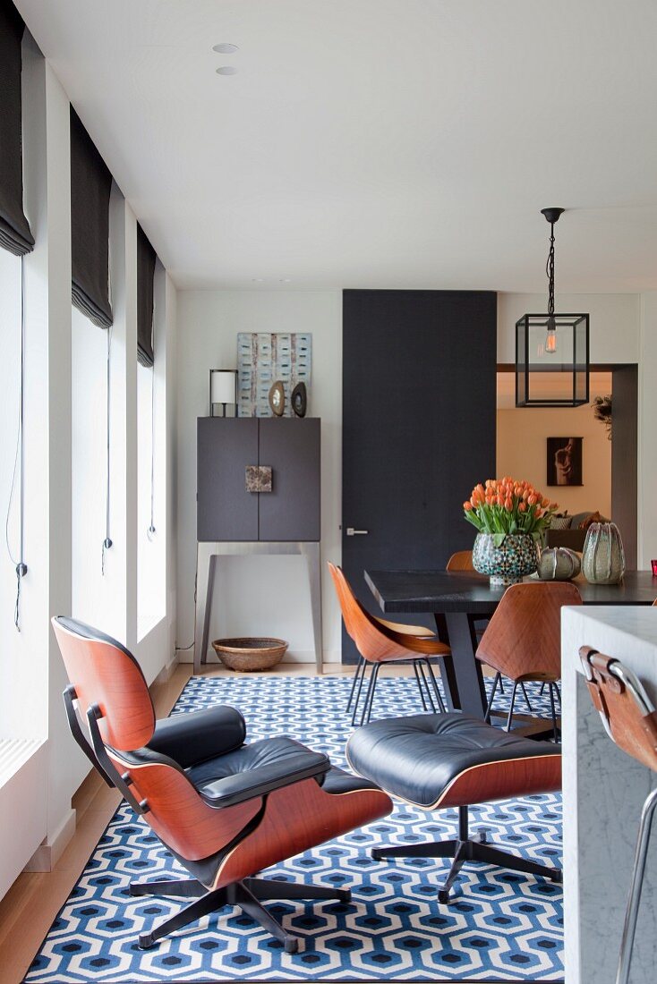 Klassiker Lounge Chair mit passendem Fussschemel auf Retro Teppich mit geometrischem Muster, im Hintergrund Essplatz in modernem Ambiente