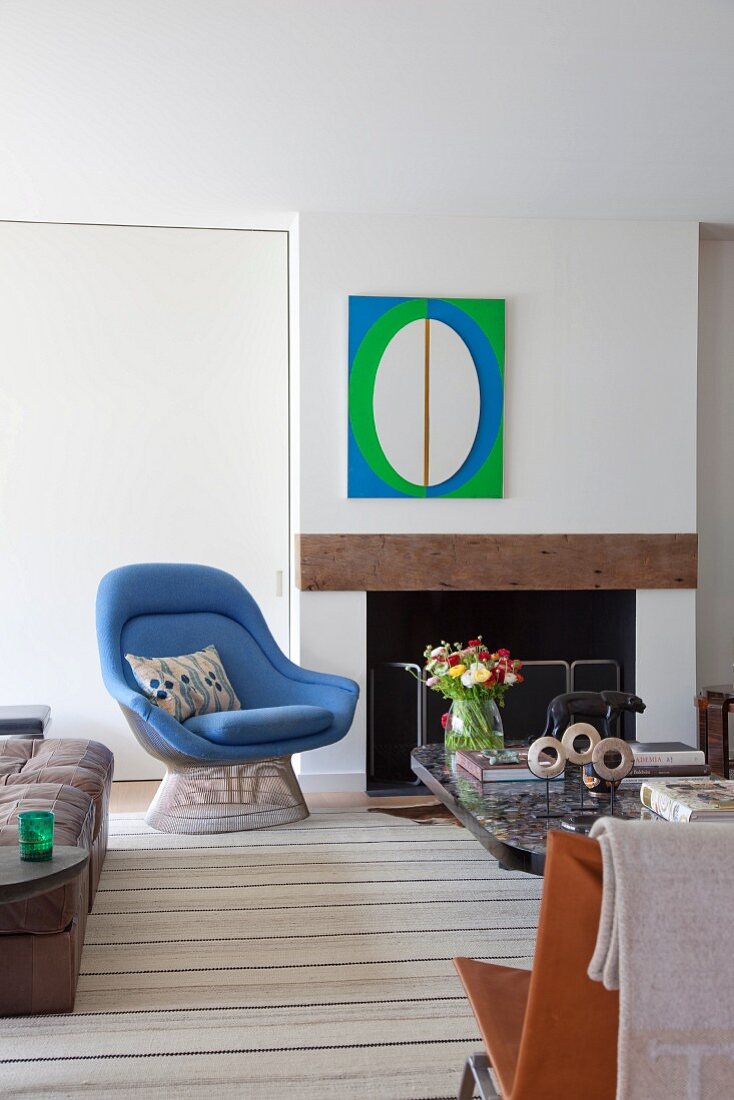 Pale blue classic armchair next to open fireplace below modern artwork in bright green, blue and white