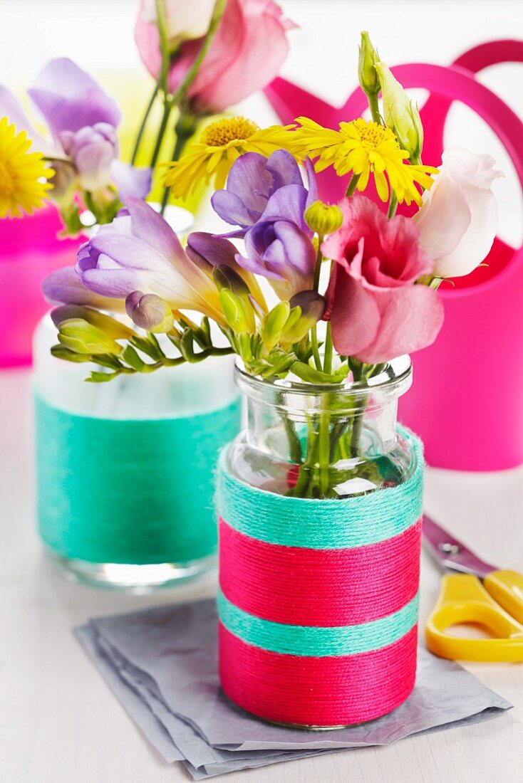 Small glass bottles wrapped in colourful woollen yarn used as vases