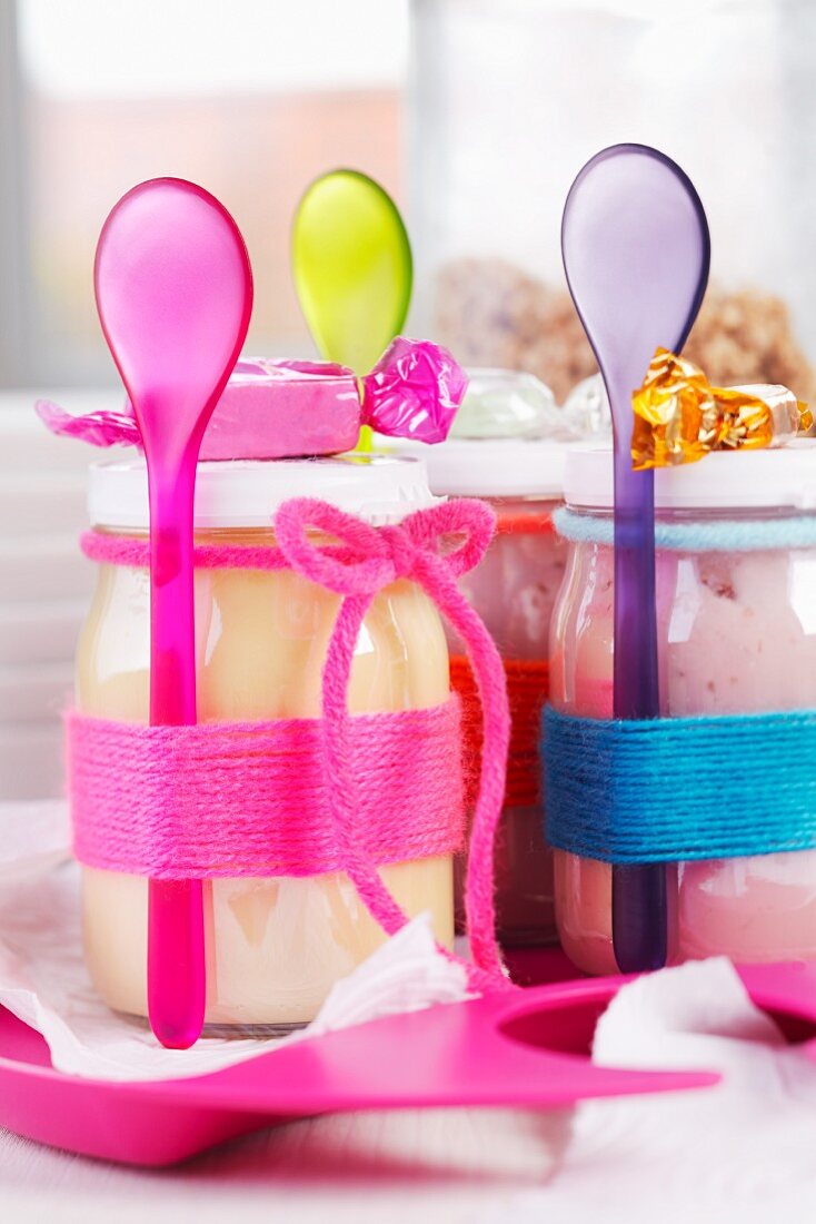 Jars of yoghurt and plastic spoons wrapped in colourful woollen yarn