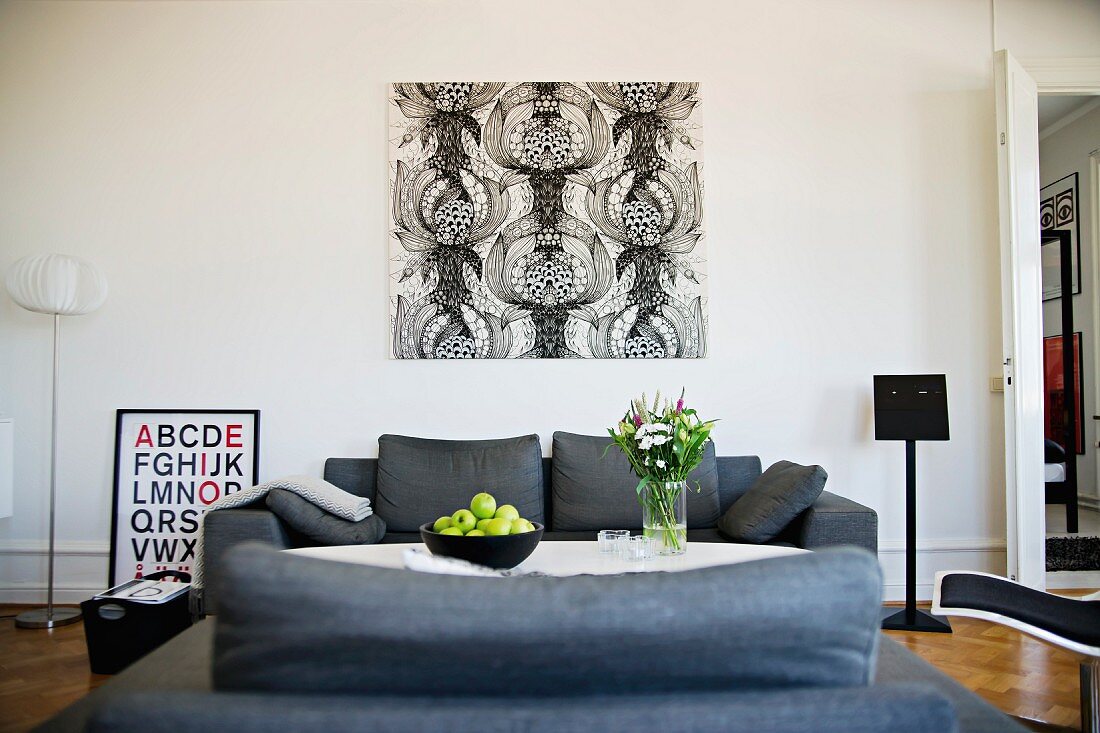 Black and white, graphic artwork on wall behind grey sofa set