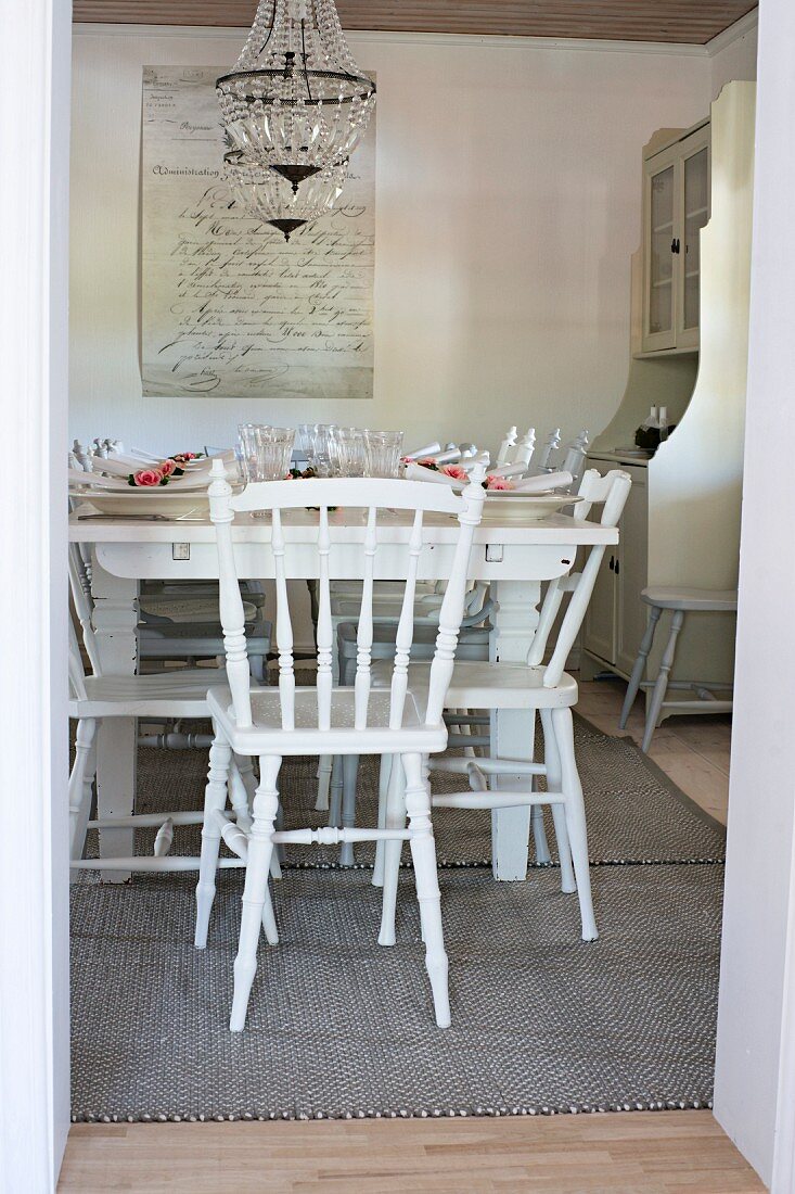 Blick durch offene Tür auf gedeckten Tisch und weiße Holzstühle in ländlichem Esszimmer