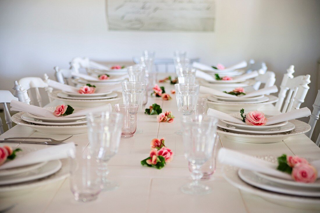 weiße Gedecke mit Rosenblüten und Stoffserviette auf weißem Holztisch