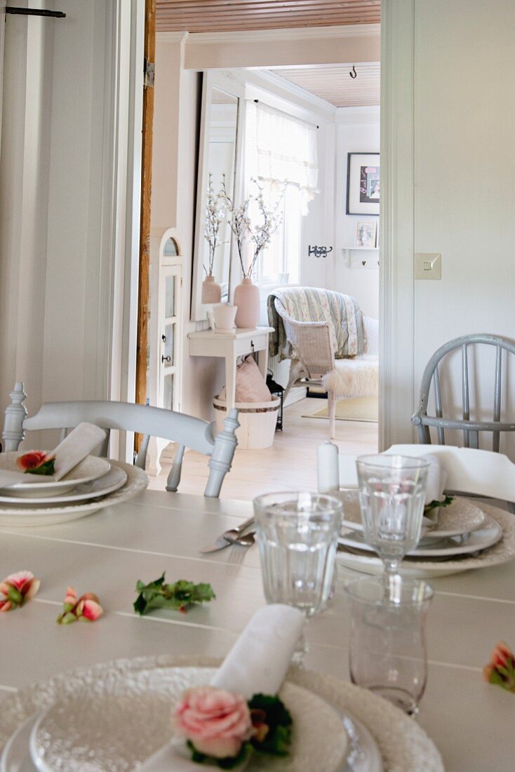 Place settings and roses on white dining table; view into rustic living room through open door in background